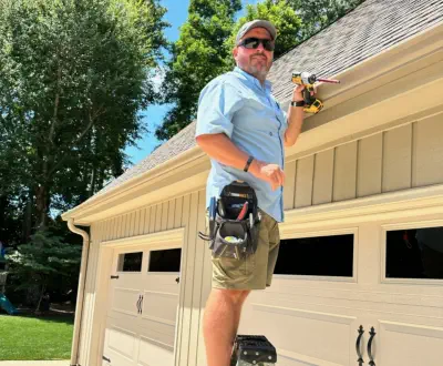 Mike Burroughs, owner of Burroughs Roofing, standing on a ladder inspecting the roof of a home.