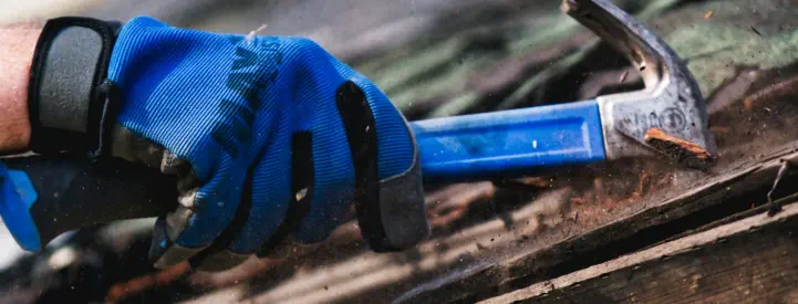 A roofing contractor with a hammer removes damaged roofing material with a hammer